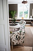 Blick durch offene Tür auf Sessel mit stilisiertem Blattmuster, im Wohnraum mit ländlichem Flair