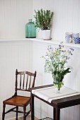 Wiesenblumenstrauss in Glasvase auf Wandtisch, seitlich antiker Holzstuhl