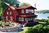 Schwedisches, historisches Holzhaus mit roter Fassade in parkähnlichem Garten am Meer