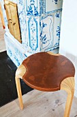 Scandinavian, laminate-wood stool with leather seat in front of antique tiled stove with classic blue and white pattern