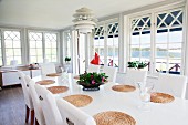 Conservatory ambiance in Swedish country house with classic, Scandinavian lamp above oval dining table with round, raffia place mats