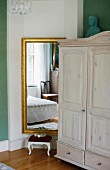 Pale farmhouse cupboard next to gilt-framed mirror on wall and small foot stool