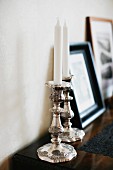 White candles in silver candlesticks on top of chest of drawers