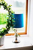 Table lamp with blue fabric lampshade next to potted ivy topiary on windowsill