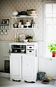 Half-height cabinet painted white below crockery on bracket shelves in rustic kitchen