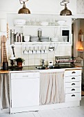 Functional kitchen counter with integrated dishwasher and drawers below cups and crockery on white, wall-mounted shelves