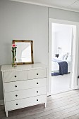 White chest of drawers next to open bedroom door with view of double bed