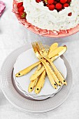 Gold dessert cutlery with fish motif on stacked plates next to strawberry cream cake