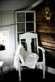 Lace blanket on white-painted chair with seat cushion in corner of wood-clad attic room
