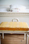 Antiker Hocker im Regency Stil, weiss lackiert, Sitzpolster mit goldgelb gemustertem Bezug an Bettende