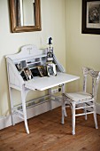 Vintage, fold-down writing desk painted white and kitchen chair with upholstered seat in corner of room painted yellow