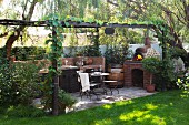 Outdoor kitchen on terrace with pergola, seating area and pizza oven in well-tended garden