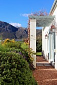 Pergola on masonry columns adjoining Mediterranean country house with mountainous landscape in background