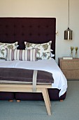 Wooden bench with seat cushion at foot of double bed with button-tufted headboard