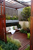 Peaceful oasis on planted wooden deck with scatter cushions on bench and wooden slatted pergola