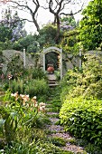 Sonnenbeschienener Garten mit Weg aus einzelnen Platten, im Hintergrund Gartenzaun aus Holzgitter