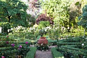 Urn at intersection of gravel paths between flowerbeds edged in low hedges in sunny garden