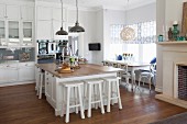 Free-standing island counter and white bar stools in open-plan, country-house kitchen with dining set below window