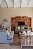 Scatter cushions on upholstered and wicker sofas in front of flatscreen TV mounted on exposed brick back wall of former fireplace