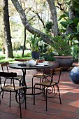 Gartenstühle und verschnörkeltes Tischgestell auf einer Terrasse unter Bäumen