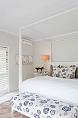 Doppelbett mit weißem Himmelgestell, an Bettende gepolsterte Bank mit floralem, weiss-blauem Muster, in elegantem Schlafzimmer