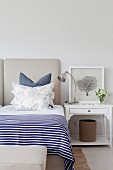Double bed with blue and white striped bedspread, arranged scatter cushions and white-painted bedside table