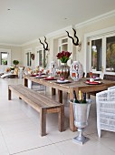 Long, set wooden table and wooden bench and metal urn used as wine cooler on roofed veranda