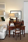 Antique chair and bureau made from dark wood, table lamp with pale lampshade and white sofa