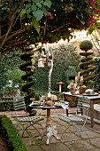 Festively set bistro table on terrace and buffet on table between topiary bushes in garden