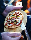Mann hält Holzbrett mit Minipizza