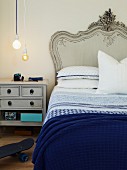 Bed with curved headboard painted pale grey, white and blue bed linen and matching bedside cabinet below simple pendant lamps