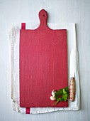 Garlic and parsley on a red wooden chopping board on a tea towel next to a knife