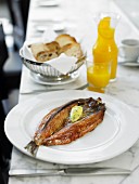Smoked herring with herb butter with white bread and orange juice in the background