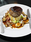 A beef medallion on a bed of mashed potatoes and parsnips with gravy and shallots