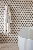 Gerundete Badewanne vor Wand mit wabenartigem Muster in Weiß- und Brauntönen