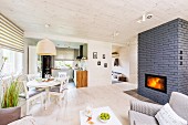 Pale, open-plan interior with fireplace built into grey brick partition and dining area below rattan pendant lamp