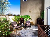 Rattan Outdoorstühle auf Natursteinboden einer Terrasse, teilweise berankte Mauer