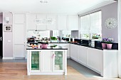 An elegant fitted kitchen with white cupboards and lilac accessories on shiny work surfaces