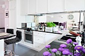 Moderne Einbauküche mit polierten schwarzen Arbeitsflächen und Spiegel-Rückwand; Lederhockern an der Frühstücksbar
