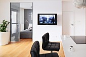 Black leather stools at a breakfast bar with a flatscreen television on the wall next to the bedroom door