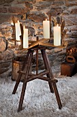 Old wooden reel with four candles used as Advent wreath on flokati rug in front of stone wall