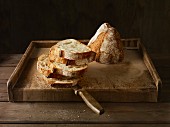 A halved loaf of artisan bread, half sliced, on a wooden board
