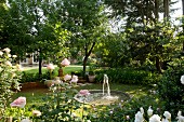 Von Bäumen und Rosenstauden (Iceberg, Gloria Dei) umgebenes Teichbecken mit Springbrunnen in weitläufigem Gartengrundstück