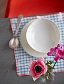 A view of a place setting with a soup bowl and flowers in a vase
