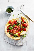 Pizza with pesto, tomatoes, bacon and herbs on a chopping board