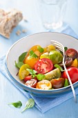 A colourful tomato salad with a chunk of bread an basil leaves
