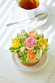 A cupcake with romantic sugar flowers in front of a cup of tea