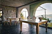Tisch mit antiken Porzellanterrinen und Esstisch mit modernen Schalenstühlen vor Panoramafenstern mit Meerblick