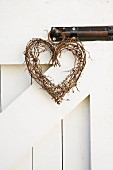 A heart-shaped wreath made from willow twigs hanging from a bolt on a wooden gate