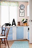 Simple, nostalgic country-house kitchen in pale blue and white with various wooden chairs